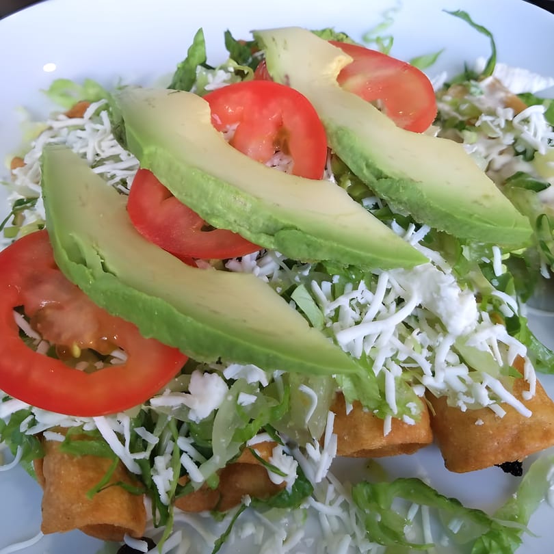 Crispy taquitos from Sol Azteca, topped with fresh lettuce, shredded cheese, sliced tomatoes, and avocado.